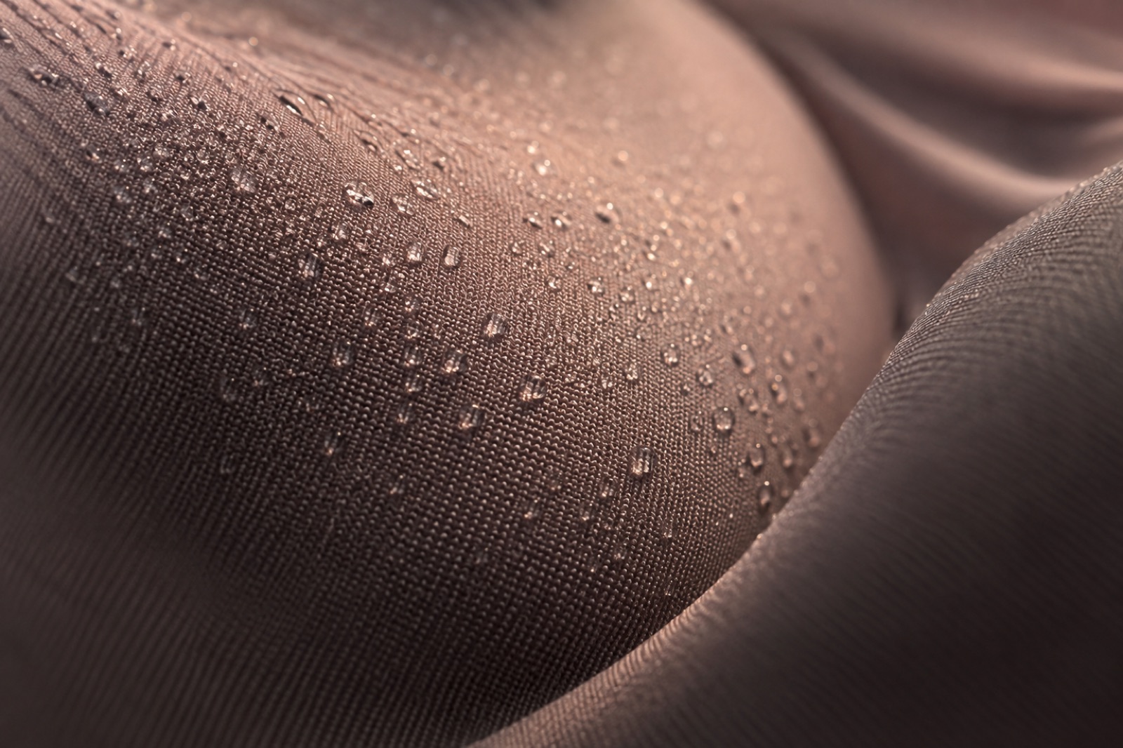 Close-up of tiny water droplets beaded across the folds of a tightly woven brown synthetic fabric