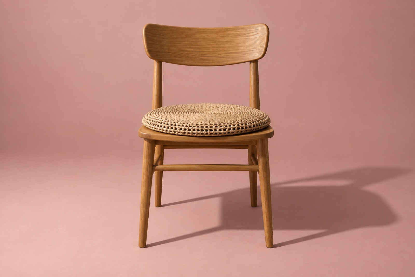 A wooden chair against a pink wall with a round knit cushion full of holes on the seat