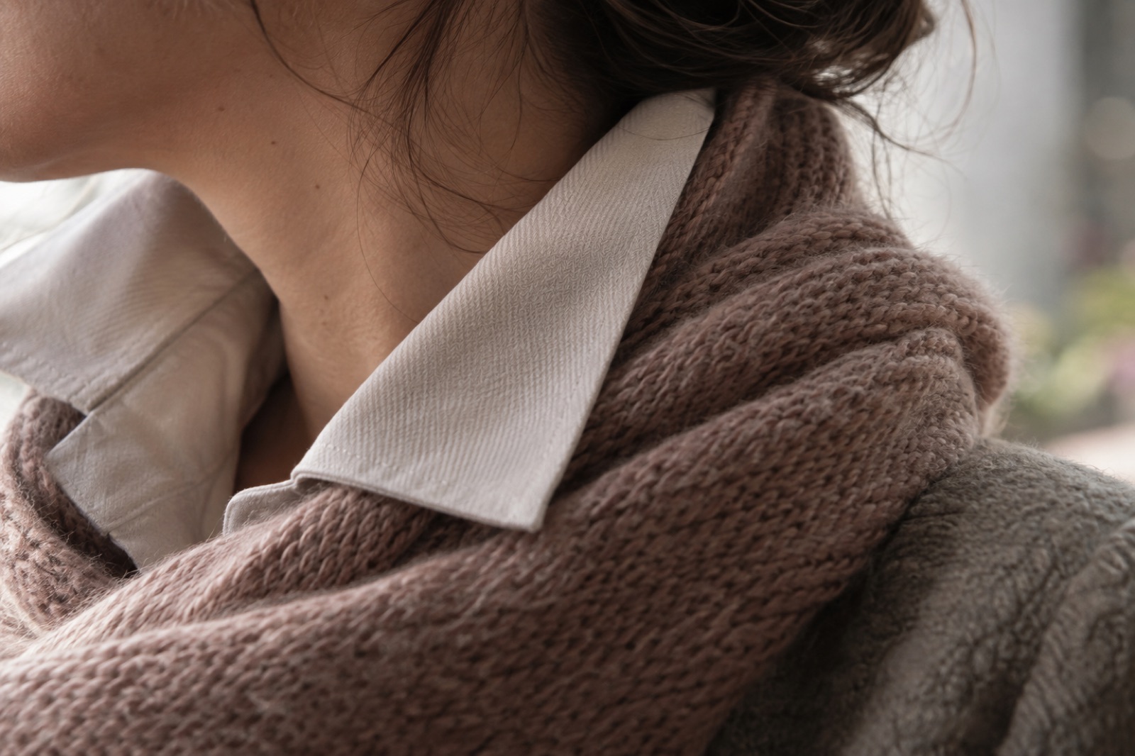 A neck turned to the side, with a light shirt collar standing up and a brown knit scarf wrapped over it
