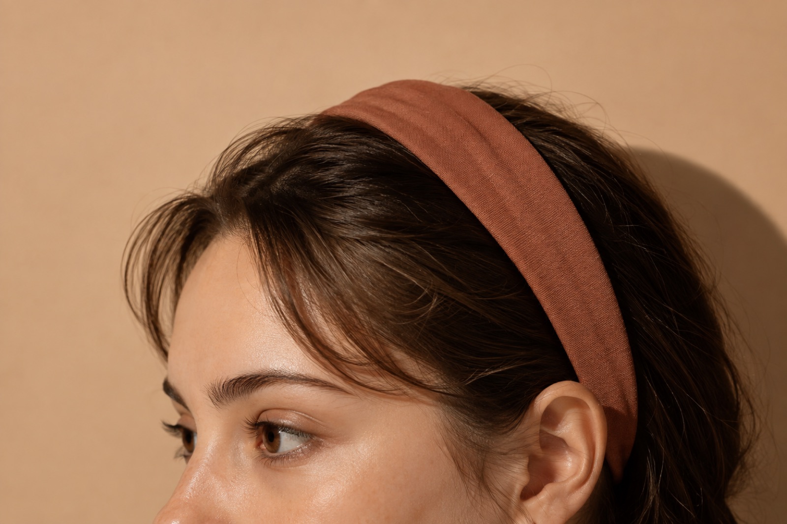Gilid na anyo ng babaeng may brick-red na telang headband sa harap ng pader na kulay aprikot, may ilang hibla ng bangs na nakalaylay sa gilid ng noo