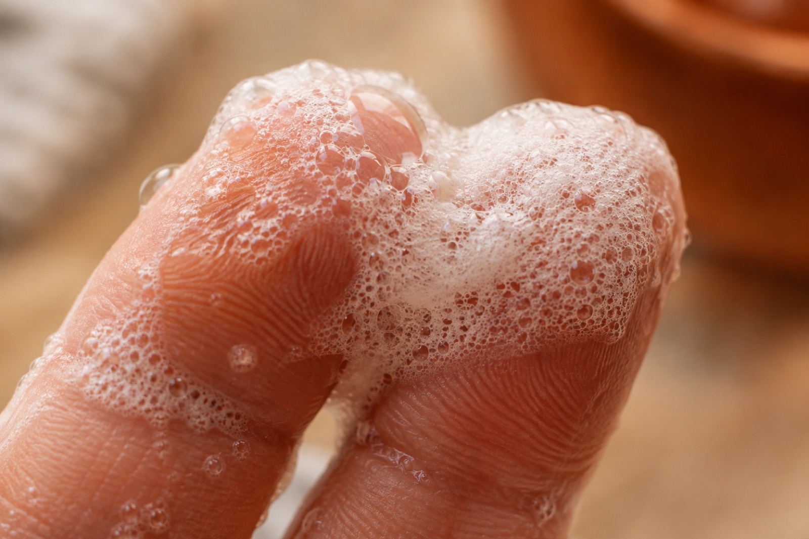 Close-up of dense white soap lather with tiny bubbles resting on two fingertips