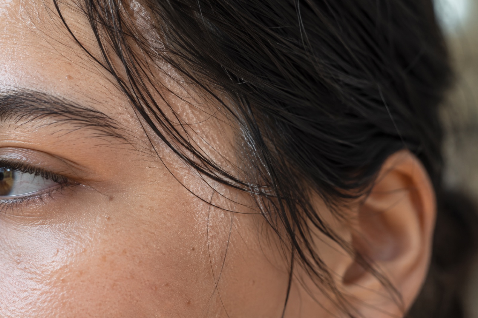Close-up of the side of a face from eye to ear, with strands of damp-looking black hair falling over the temple